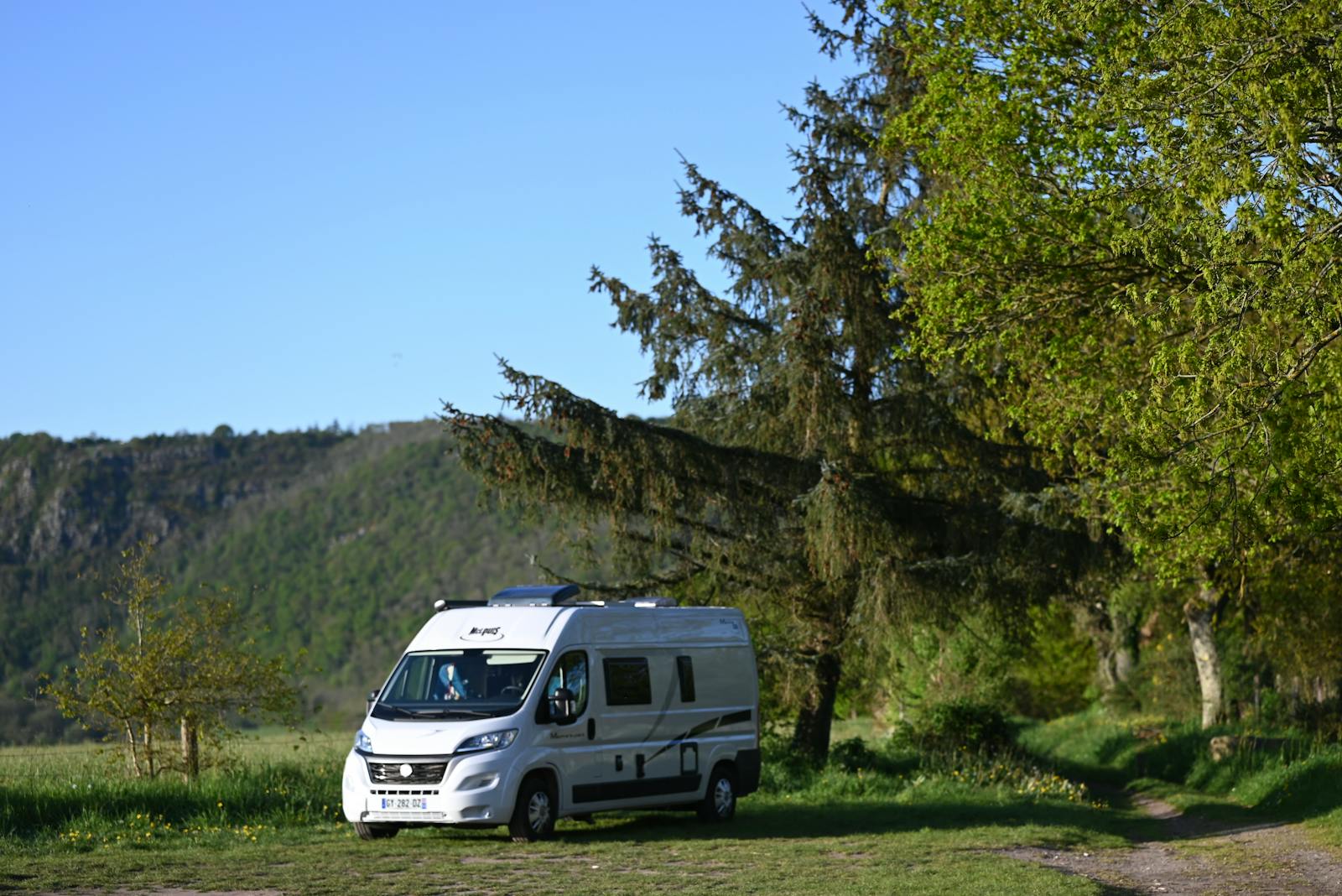 A camper van parked in a lush green landscape with clear skies, perfect for outdoor adventures.